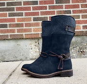 Navy blue suede winter boots with a felt collar and decorative lace, set against a brick wall background.