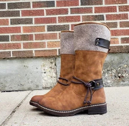 Stylish brown suede winter boots with grey fabric upper and decorative strap on a concrete surface.